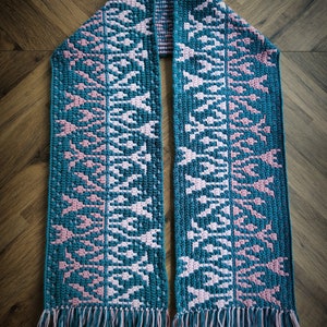 May include: A teal and pink crocheted scarf with a geometric pattern and fringe on the ends.