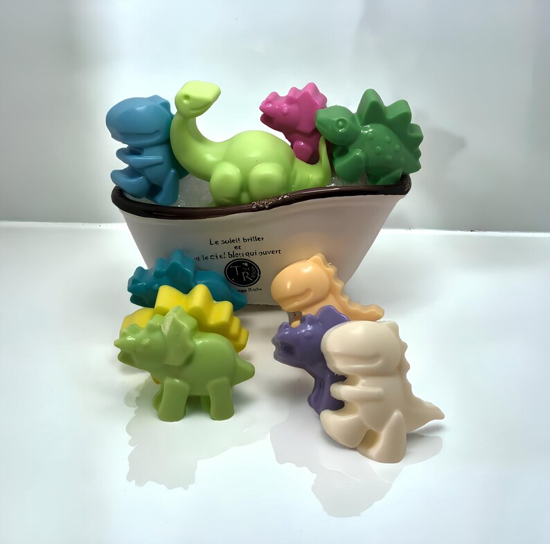 May include: A set of colorful dinosaur-shaped bath toys. The toys are made of a soft, rubbery material and are perfect for bath time fun. The toys are in a white ceramic boat with the text "Le soleil brille... et le ciel!  Heureux ouvert" on the side.