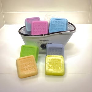 May include: A white ceramic tub filled with colorful square-shaped soaps. The soaps are all labeled "100% Hand Made".