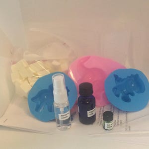 May include: A craft kit for making soap with a variety of supplies, including white soap base, two silicone molds shaped like dinosaurs, a bottle of isopropyl alcohol, a bottle of fragrance oil labeled "Pear", and a small bottle of green soap color.