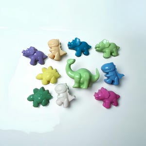 May include: A collection of ten colorful dinosaur figurines made of a smooth, solid material. The dinosaurs are in various poses and include a green brachiosaurus, a purple triceratops, a yellow stegosaurus, a blue triceratops, a green ankylosaurus, a white tyrannosaurus rex, a green triceratops, a white stegosaurus, a blue tyrannosaurus rex, and a pink triceratops.
