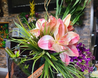 May include: A glass vase with a brown leather strap around the top, filled with pink and white flowers, green leaves, and purple flowers.