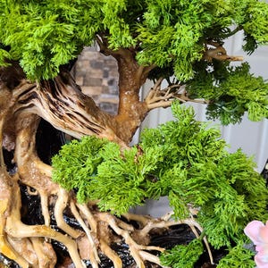 May include: A detailed bonsai tree sculpture with vibrant green foliage and a textured brown trunk and roots. The tree is set in a black pot, with a naturalistic design. The overall aesthetic is a blend of nature and art.