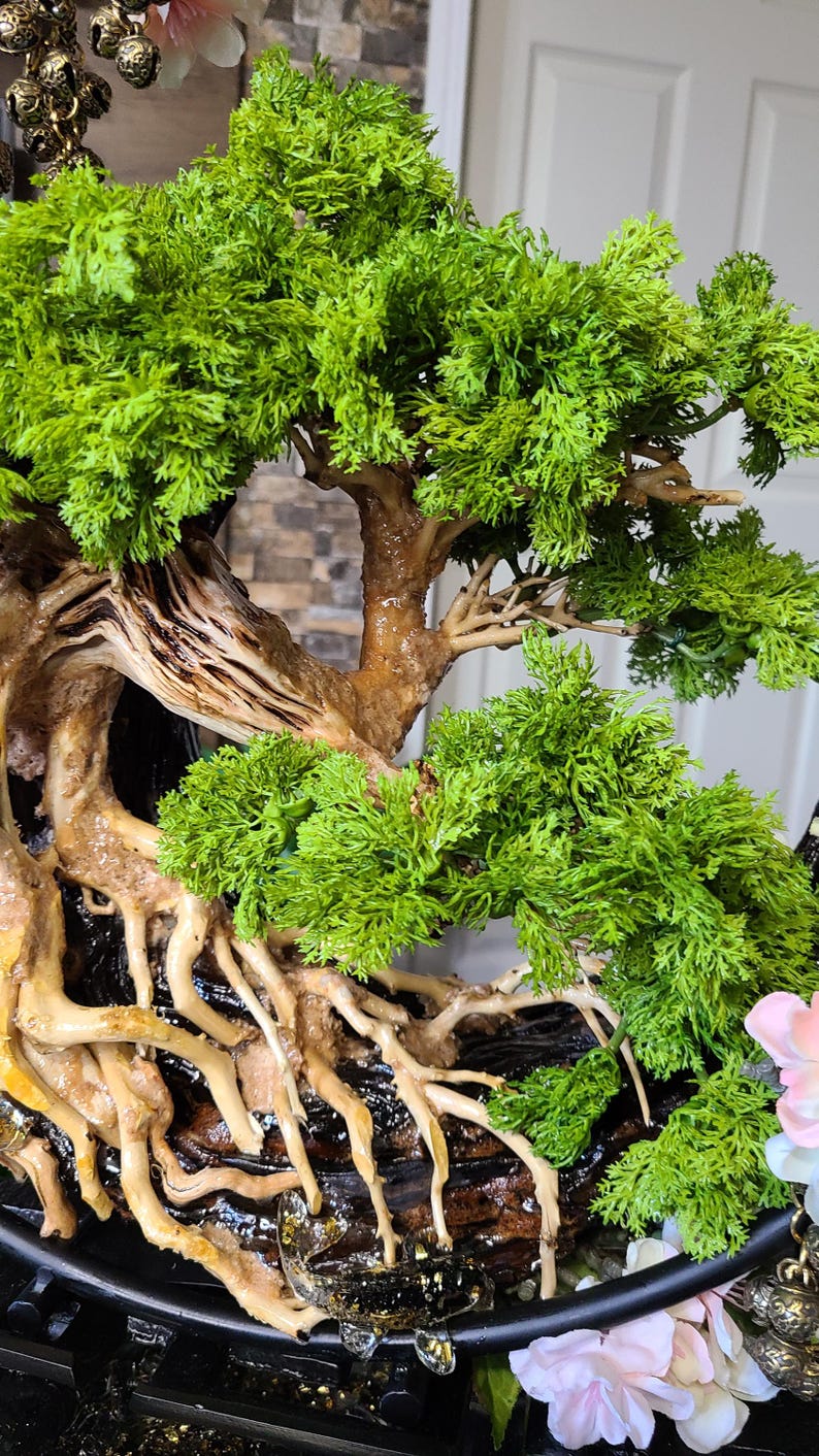 May include: A detailed bonsai tree sculpture with vibrant green foliage and a textured brown trunk and roots. The tree is set in a black pot, with a naturalistic design. The overall aesthetic is a blend of nature and art.