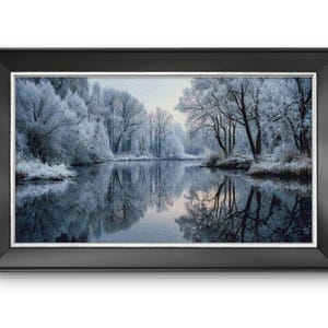 May include: A framed print of a winter landscape. The image shows a tranquil river reflecting snow-laden trees and a pale sky. The black frame has a silver inner border, contrasting with the cool colours of the scene.