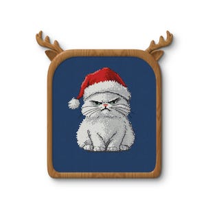 May include: A cross-stitch of a grumpy white cat wearing a red Santa hat, set against a blue background. The artwork is framed in a wooden rectangle with decorative antler accents, perfect for holiday decor.
