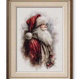 May include: A framed cross-stitch portrait of Santa Claus. Santa is depicted in profile, wearing a red hat and coat with white fur trim. His long white beard and rosy cheeks are visible. The background has a snowy effect.