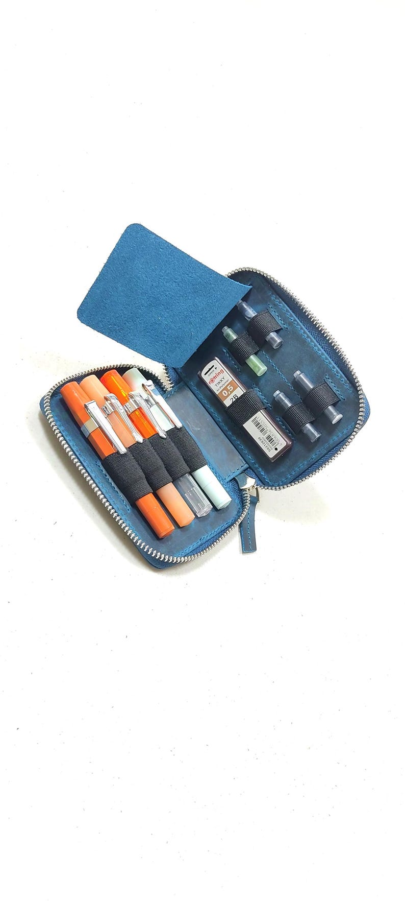 May include: A blue leather zippered case with multiple slots for pens and ink cartridges. The case is open and shows a variety of pens and cartridges, including a red and orange pen, a black pen, and a green pen.