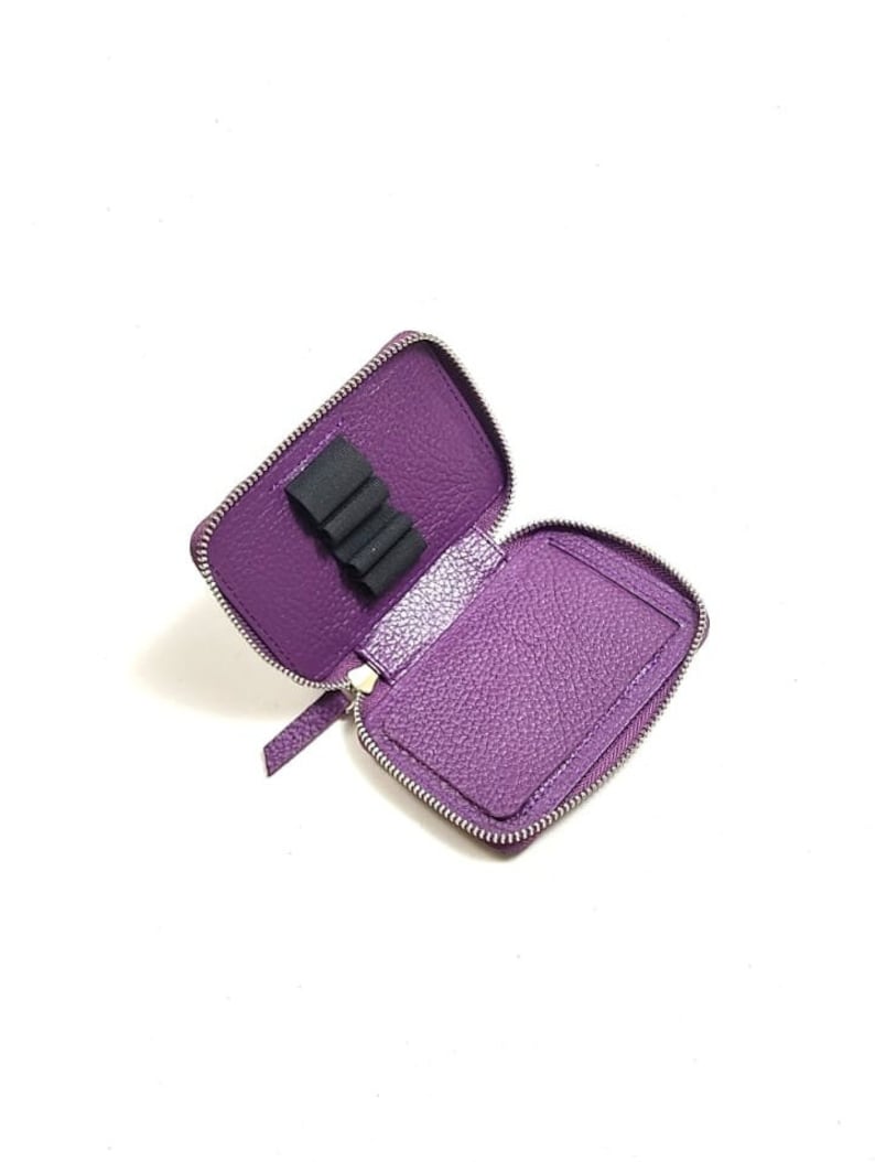 May include: A purple leather zippered pouch with a black elastic band inside for holding pens or pencils.