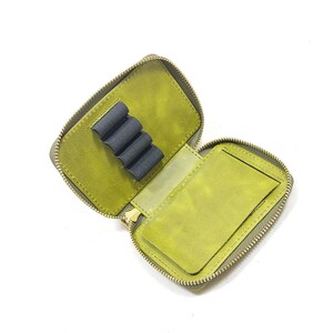 May include: Open, olive green leather pencil case with a zipper closure. The interior features a pen holder and a small pocket. The case is designed to hold pens, pencils, and other small stationery items.
