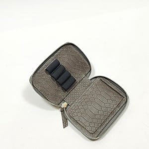 May include: A gray zippered pouch with a faux snakeskin pattern. The pouch is open and has a black elastic band inside to hold items.