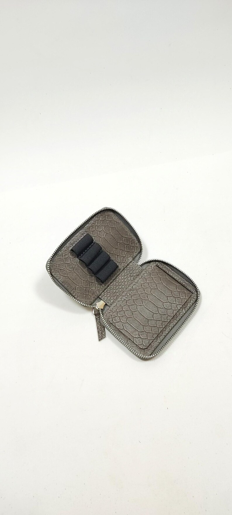 May include: A gray zippered pouch with a faux snakeskin pattern. The pouch is open and has a black elastic band inside to hold items.