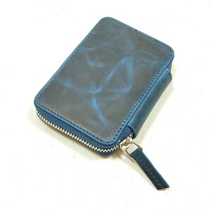 May include: A small, dark blue leather wallet with a zipper closure. The wallet has a distressed look and a subtle marbled pattern.