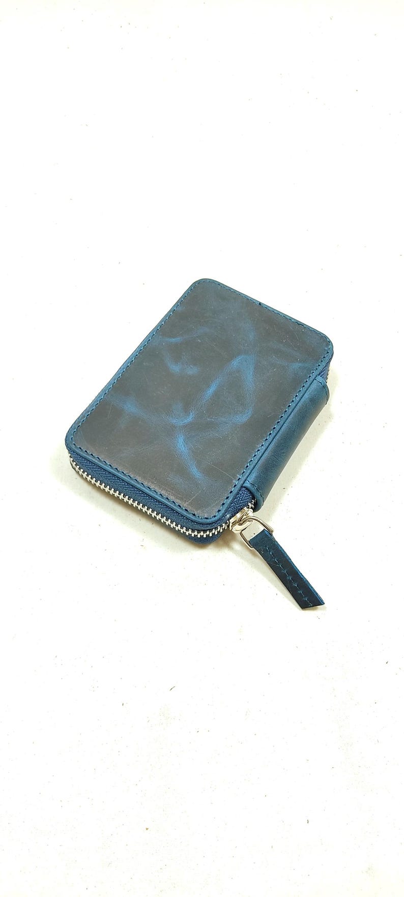 May include: A small, dark blue leather wallet with a zipper closure. The wallet has a distressed look and a subtle marbled pattern.