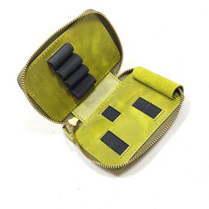 May include: Open, olive green leather pencil case with a gold zipper. The interior features black elastic loops and two black rectangular pockets. The case is designed to hold pens, pencils, or other small items.