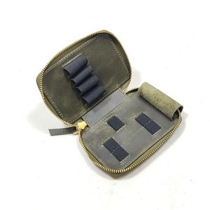 May include: A small, green leather zippered pouch with multiple slots for holding small items. The pouch is open and the interior is gray with black elastic bands.