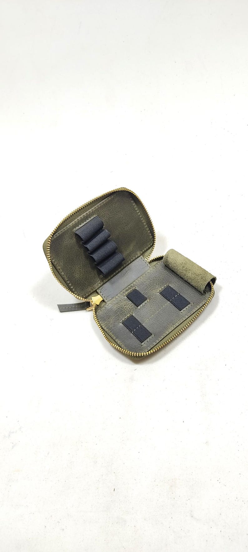 May include: A small, green leather zippered pouch with multiple slots for holding small items. The pouch is open and the interior is gray with black elastic bands.