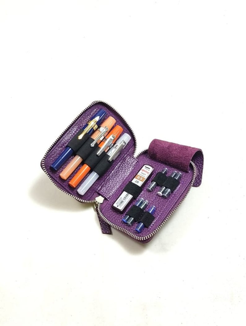 May include: A purple leather zippered pouch with a variety of pens, pencils, and ink cartridges inside. The pouch is open and the contents are visible.