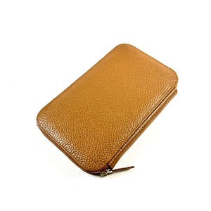 May include: A rectangular, tan-colored wallet with a textured surface. The wallet has a zipper closure and a small, attached zipper pull. The wallet is made of a leather-like material and is set against a white background.
