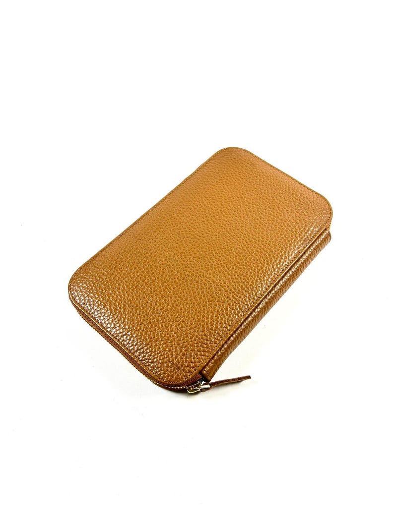 May include: A rectangular, tan-colored wallet with a textured surface. The wallet has a zipper closure and a small, attached zipper pull. The wallet is made of a leather-like material and is set against a white background.