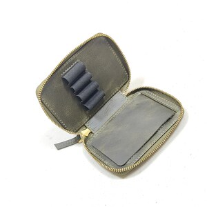 May include: A small, green leather zippered pouch with a gold zipper. The pouch has a separate compartment for holding pencils or pens.