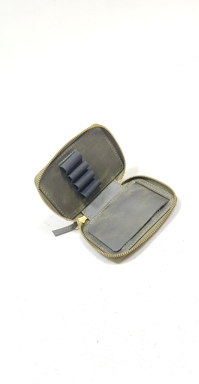 May include: A small, green leather zippered pouch with a gold zipper. The pouch has a separate compartment for holding pencils or pens.