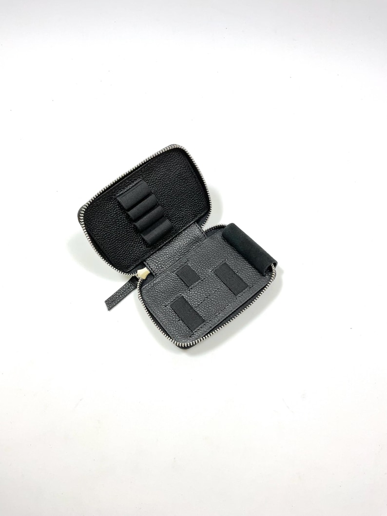 Pu&ograve; includere: Un astuccio nero aperto con cerniera e esterno strutturato. L'interno presenta scomparti e cinghie elastiche per organizzare piccoli oggetti. L'astuccio &egrave; progettato per contenere penne, matite o altri accessori. La cerniera &egrave; argentata.