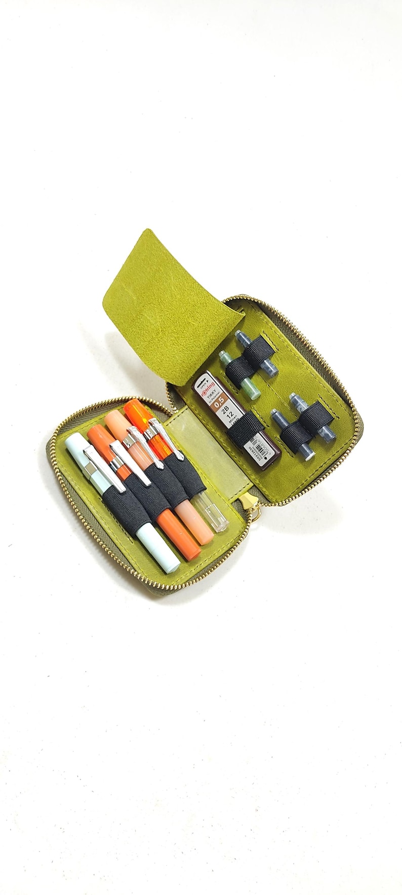 May include: Open, lime green leather pen case with a zipper closure. The case contains several pens in various colors, including orange, white, and light blue. Also included are mechanical pencils and lead refills. The case is open, revealing its contents.