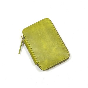 May include: A small, rectangular, olive green leather wallet with a zipper closure. The wallet has a textured surface and a gold-colored zipper. The zipper pull is made of the same leather as the wallet.