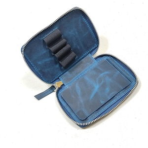 May include: A blue leather zippered pouch with a pen holder and a separate pocket. The pouch is open and the zipper is partially unzipped.