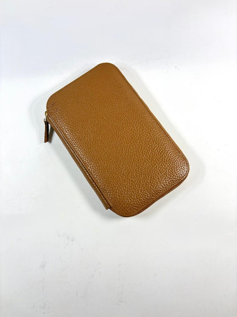 May include: A rectangular, brown leather wallet with a zipper closure. The wallet has a textured surface and a rounded top. The zipper pull is a darker shade of brown.