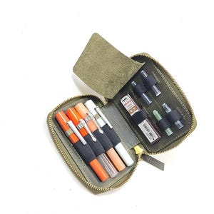 May include: A green leather zippered pouch with multiple compartments for pens, pencils, and other writing tools. The pouch is open and the compartments are filled with various writing instruments.
