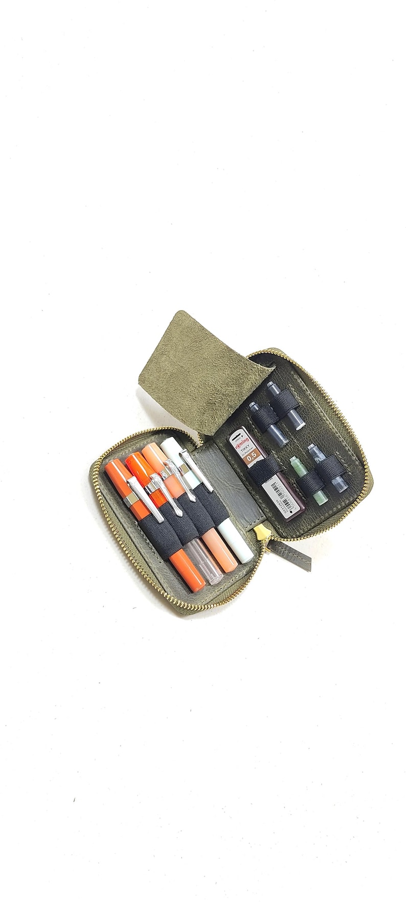 May include: A green leather zippered pouch with multiple compartments for pens, pencils, and other writing tools. The pouch is open and the compartments are filled with various writing instruments.