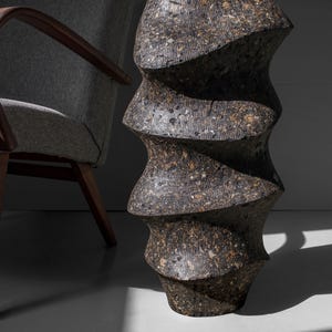 May include: A dark gray ceramic vase with a unique, twisted, and textured design. The vase has a rough, uneven surface and a spiral shape.