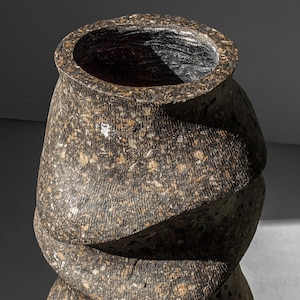 May include: A brown and black ceramic vase with a textured surface and a swirling design. The vase is empty and has a wide opening at the top.