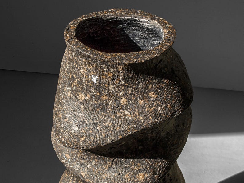 May include: A brown and black ceramic vase with a textured surface and a swirling design. The vase is empty and has a wide opening at the top.