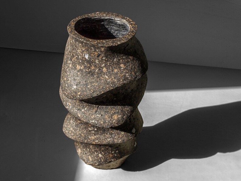 May include: A brown ceramic vase with a textured, speckled surface. The vase has a unique, twisted shape with multiple layers.