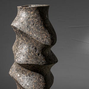 May include: A tall, dark gray ceramic vase with a unique, twisted, and textured design.