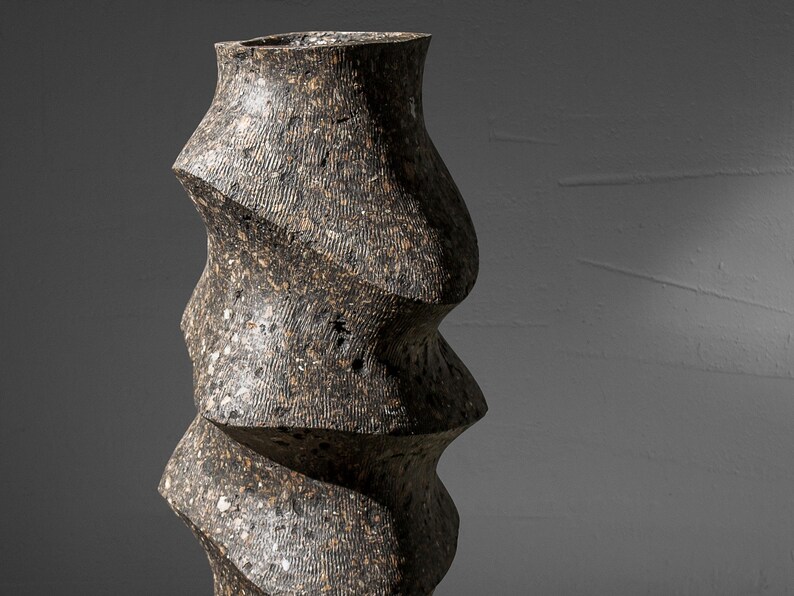 May include: A tall, dark gray ceramic vase with a unique, twisted, and textured design.