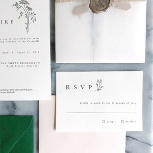 May include: A white RSVP card with green floral accents. The text reads "RSVP" in a large font and "kindly respond by the fifteenth of july" in a smaller font. There are two checkboxes below the text, one labeled "accepts" and the other labeled "declines".