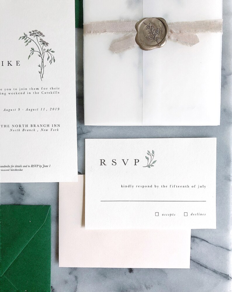 May include: A white RSVP card with green floral accents. The text reads "RSVP" in a large font and "kindly respond by the fifteenth of july" in a smaller font. There are two checkboxes below the text, one labeled "accepts" and the other labeled "declines".