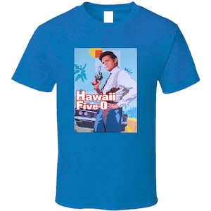 May include: A blue t-shirt with a graphic of a man holding a gun and the text "Hawaii Five-0" in red and white letters.