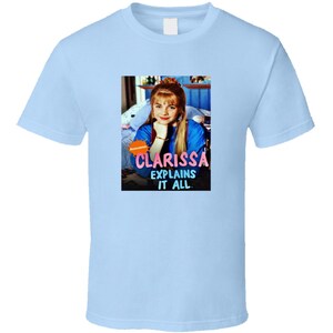May include: A light blue t-shirt with a picture of Clarissa from the Nickelodeon show "Clarissa Explains It All". The image is in a square frame with the show's title in pink and white letters.
