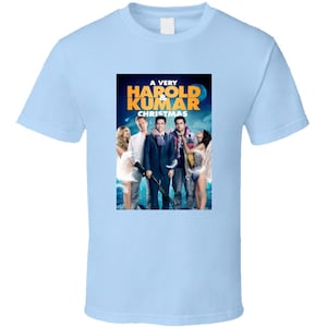 May include: A light blue t-shirt with a graphic of the movie poster for "A Very Harold & Kumar Christmas". The poster features the four main characters from the movie, Harold, Kumar, Maria, and Nisha, standing in front of a snowy background.