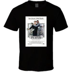 May include: A black t-shirt with a white print of the movie poster for Trading Places. The poster features Dan Aykroyd and Eddie Murphy, with the text "Dan Aykroyd Eddie Murphy They've not just getting rich... They're getting even." and "Trading Places Some very funny business."