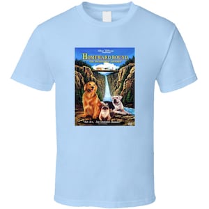 May include: A light blue t-shirt featuring a movie poster design with a golden retriever, a bulldog and a cat. The poster is for the film "Homeward Bound: The Incredible Journey".
