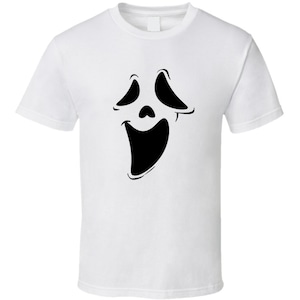 May include: White t-shirt featuring a black graphic of a ghost face with wide eyes and an open mouth. The design is a simple, bold outline, creating a striking contrast against the white fabric. This tee is perfect for Halloween or horror movie fans.