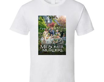 May include: White t-shirt featuring a colorful image from the TV show "Midsomer Murders." The image shows a group of people gathered around a table outdoors. The show's title is printed in a stylized font below the image.