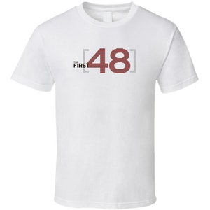 May include: White t-shirt with the text "THE FIRST [48]" printed in black and red.