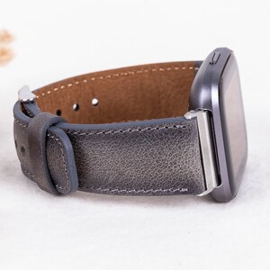 May include: A gray leather watch band with silver hardware. The band is designed for a smartwatch with a square face.